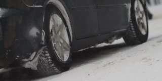 汽车正站在冬天城市里白雪覆盖的十字路口。排气管中冒出的烟雾。降雪。车轮的慢动作特写。轮胎。交通状况不佳，暴风雪。危险之旅