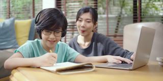 一位年轻的亚洲母亲喜欢用笔记本电脑教她的儿子做作业。亚洲小男孩很喜欢和她美丽的妈妈一起学习。