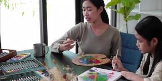 年轻的亚洲老师在美术课上和亚洲女孩一起画画。
