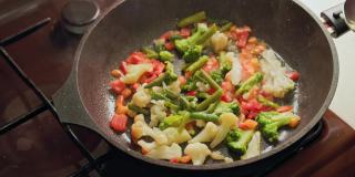 白种人的手搅拌蔬菜在煎锅与不锈钢勺子，而煎，特写