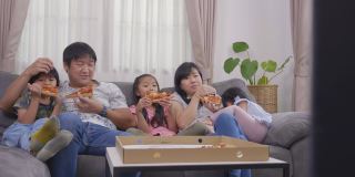 快乐的亚洲家庭喜欢在假日里坐在沙发上吃披萨和看电视