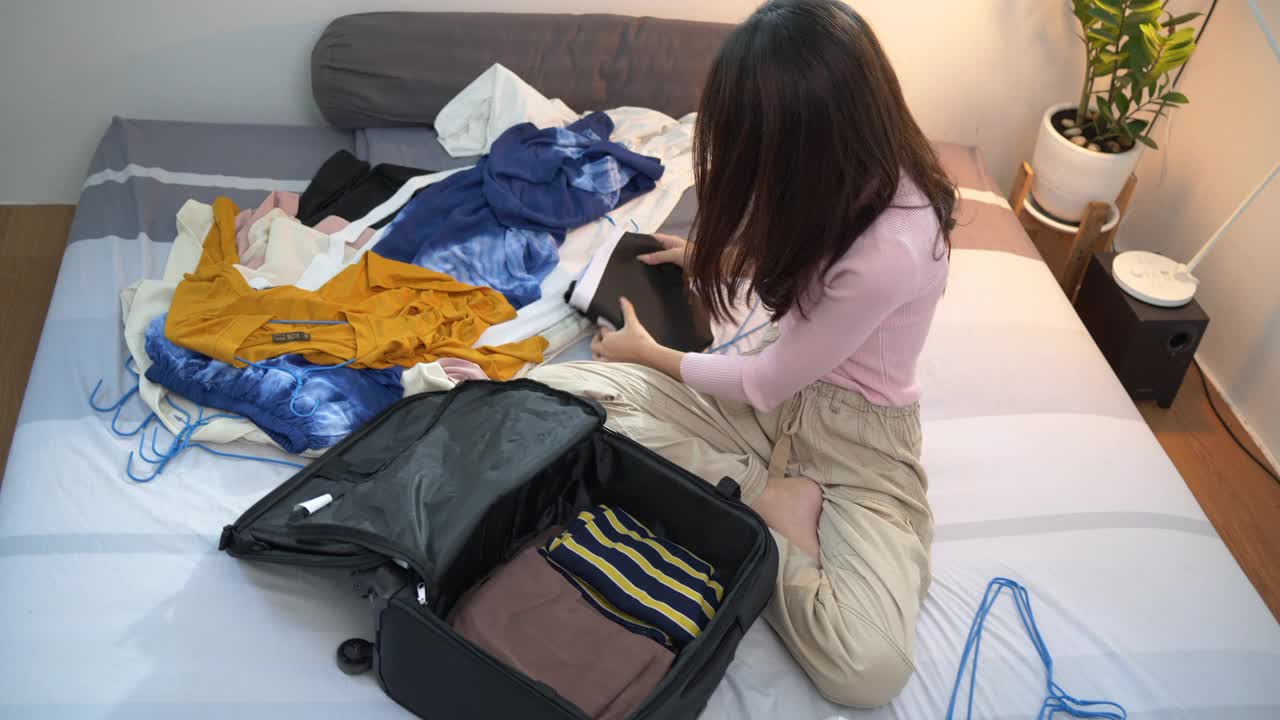 亚洲妇女在家里把衣服装进行李箱，准备旅行