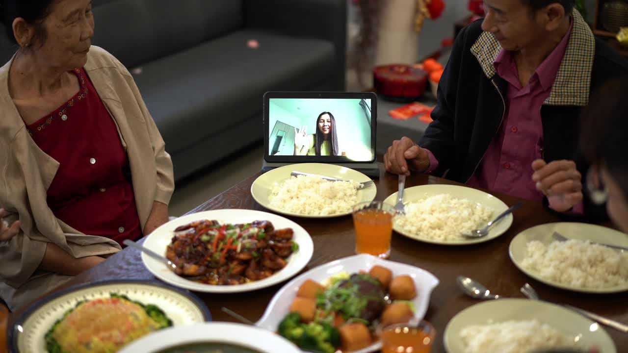 快乐的亚洲华人家庭在团圆饭期间用数码平板电脑视频给亲戚打电话