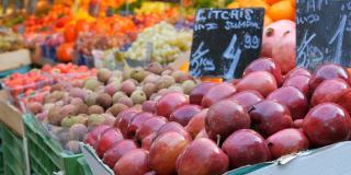 前景是大红苹果和异域水果。一个大城市的蔬菜市场。种类繁多的蔬菜和水果可供选择。健康的新鲜有机素食食品在柜台上。德语价格标签