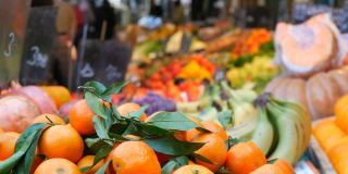 前景是有着绿叶和奇异果实的橘子。蔬菜市场。种类繁多的蔬菜和水果可供选择。健康的新鲜有机素食食品在柜台上。