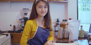 快乐的亚洲女性企业主微笑在咖啡馆柜台