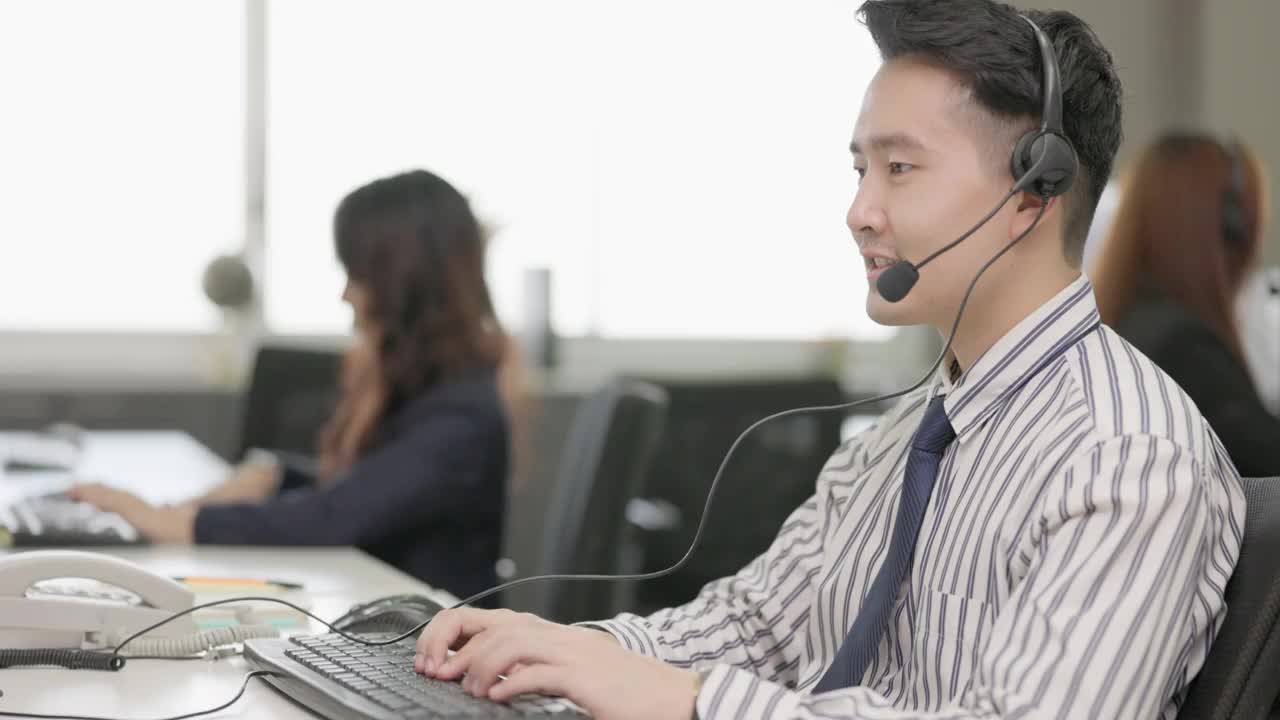 亚洲男子电话营销操作员戴着耳机与团队工作在呼叫中心城市办公室