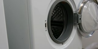 男人用手把洗好的衣服放进洗衣机。洗衣房有一台白色的大洗衣机。
