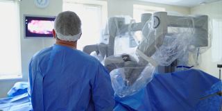 现代化手术室里的高科技设备。外科医生在医疗机器人附近的后视图。医生用机器人系统做手术，看着屏幕。