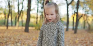 一个美丽的小女孩站在秋天的公园里，看着镜头微笑着。缓慢的运动。