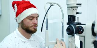 戴圣诞帽的眼科病人。一个男人在诊所测试他的眼睛。年轻男性病人检查视力。