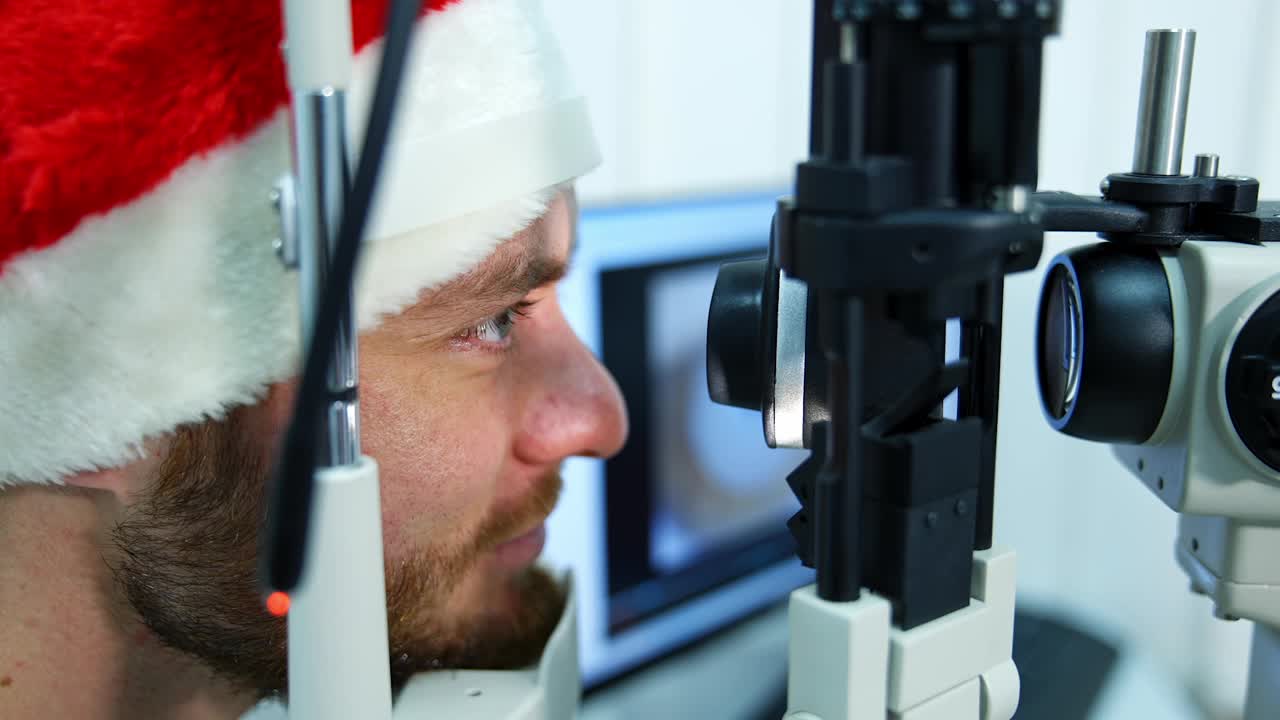 门诊治疗眼睛的病人。一个戴圣诞帽的男人的脸的侧面视图，在眼科中心看着特殊设备。特写镜头。