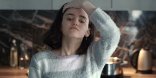 一个严肃的黑发女孩的肖像，用手拉直了头发，站在厨房的背景下
