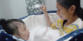 快乐的亚洲孩子们一起在家里的塑料浴缸里嬉笑，生活理念。