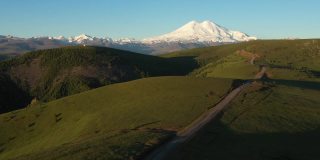 鸟瞰欧洲最高的山峰艾尔布鲁斯。俯瞰绿地、蜿蜒的道路和高加索山脉。厄尔布鲁斯山的日出