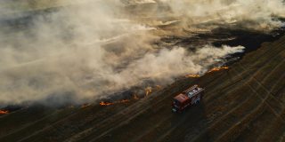傍晚，电影用干枯的胡茬和冒烟的火焰在燃烧的土地上拍摄消防车和消防员