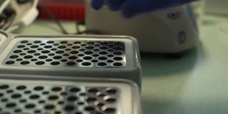 戴着医用手套、无法辨认的实验室技术人员的近距离双手将装有样本的试管放入用于DNA检测的设备中，COVID-19。