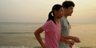亚洲儿童在沙滩上奔跑，伴以日出为背景，积极的生活理念。