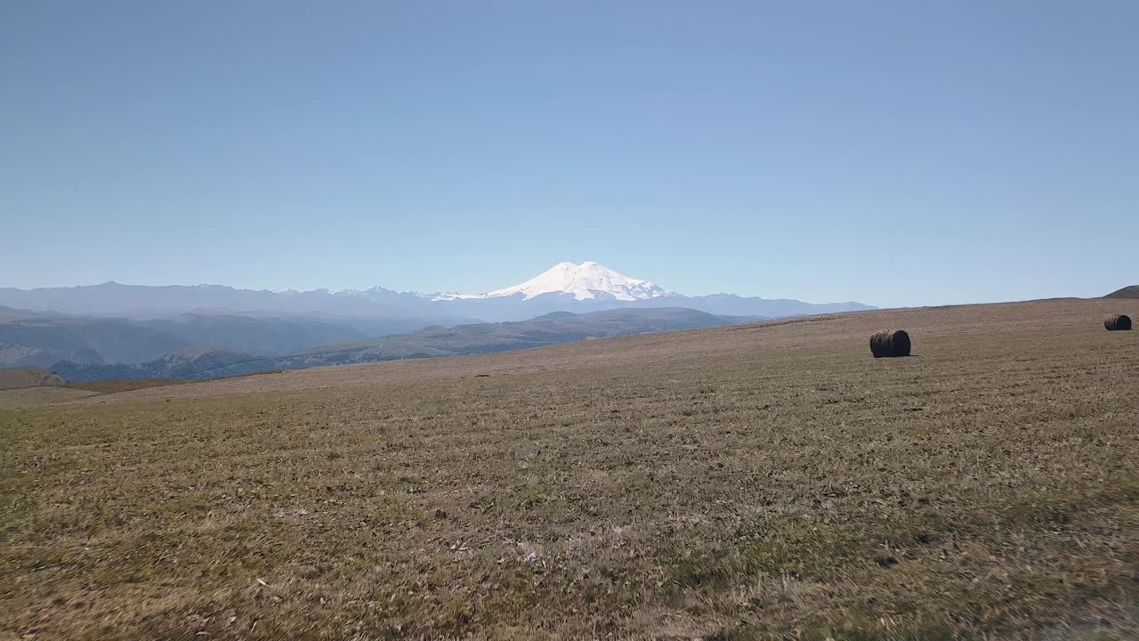 两个朋友站在田野里，一个在干草堆上，另一个在干草堆旁边。田地在高山上。周围风景美丽