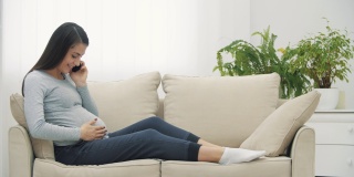 孕妇拿着手机坐在白色沙发上的4k慢动作视频。