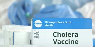 工作实验室助理旁边的桌子上放着霍乱疫苗安瓿瓶，盒子上有虚构的标志
