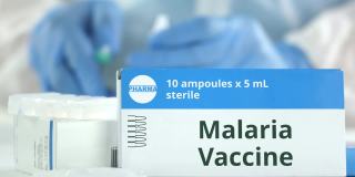 疟疾疫苗安瓿放在工作实验室助理或医生附近的桌子上，盒子上虚构的标志
