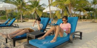 快乐的亚洲孩子戴着太阳镜在海滩椅上放松在早上在酒店或度假村度假，与家人，生活理念。
