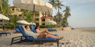 快乐的亚洲孩子戴着太阳镜在海滩椅上放松在早上在酒店或度假村度假，与家人，生活理念。