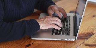 一个老人在家用笔记本电脑工作。老年人在客厅使用电脑