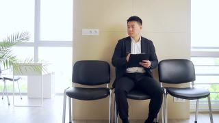 穿着商务正装的亚洲年轻人在等候室等待结果面谈或会议。在职男商人视频素材模板下载