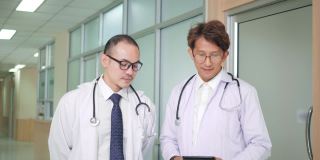 两名亚洲籍男医生，身着医务制服，站在诊所医院，面带微笑望著摄影机。