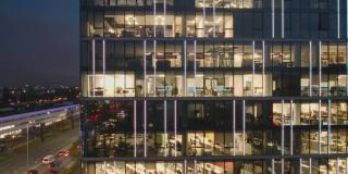 在一座现代化摩天大楼里，一架无人机对着办公人员工作到很晚的办公室的夜窗射击。