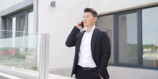 年轻的成功男人亚洲商人在阳台上一个商务办公中心讲手机