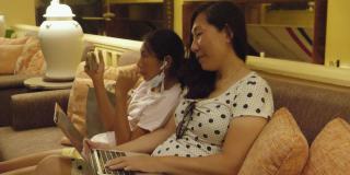亚洲母亲在酒店大堂使用笔记本电脑，在度假期间与女儿在夜间工作，在任何地方工作的生活理念。