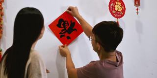 亚洲的中国夫妇装饰他们的房子，并张贴中国对联，为即将到来的中国年祝福