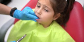 在恐惧中，勇敢的女孩，静静地坐在牙医的椅子上，而儿科牙医正在拔她的牙