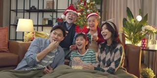 多代，亚洲幸福。一群兴高采烈的亲戚聚在沙发上，兴奋不已，妈妈、爸爸、儿子、爷爷、奶奶，穿着冬天的布艺圣诞节日服装装饰家里的圣诞树