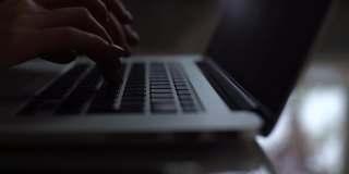 不知名的女性自由职业者在笔记本电脑键盘上打字坐在家里的办公桌上在线工作。