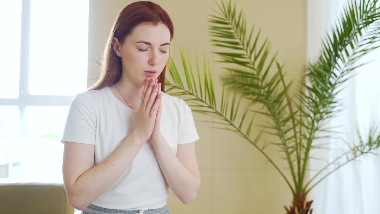 一个年轻女子在家里或室内交叉双臂真诚祈祷的特写。白人女孩或女性真诚的祈祷