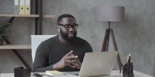 一个黑人在办公室里穿着休闲装，把手伸进笔记本电脑里，通过视频链接进行交流