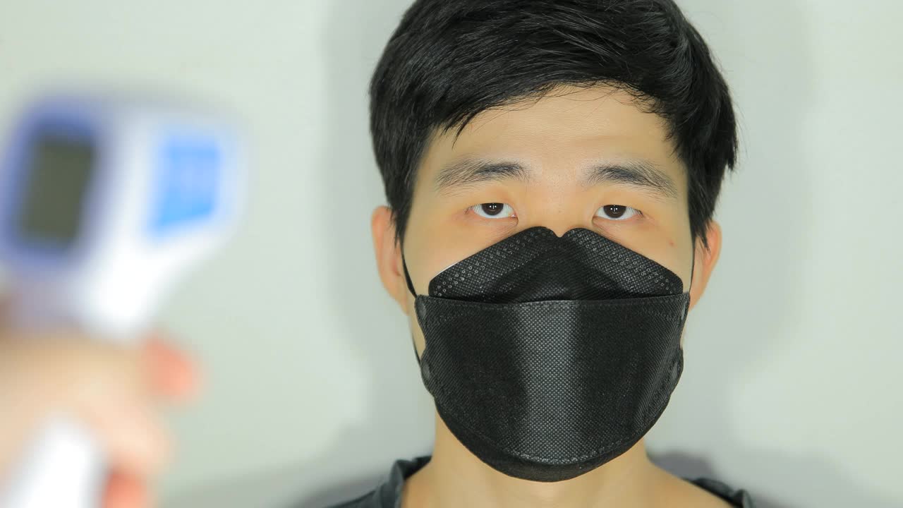 亚洲人戴着医用防护口罩等待从武汉进入办公楼前用红外测温仪测量体温。