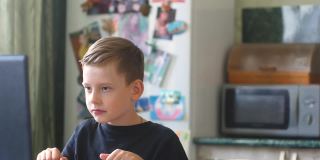 一个7-9岁的白人男孩在家里用笔记本电脑学习，在学习间隙用一个流行的玩具来缓解压力。在家给孩子们玩。这个男孩正在远程学习。本空间