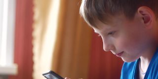 一名7 ~ 9岁的白人少年正在家中用智能手机上网。一个拿着手机的孩子的头像。网上的日常生活。有选择性的重点