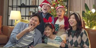 多代，亚洲幸福。一群兴高采烈的亲戚聚在沙发上，兴奋不已，妈妈、爸爸、儿子、爷爷、奶奶，穿着冬天的布艺圣诞节日服装装饰家里的圣诞树