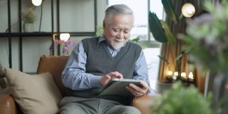 亚洲老人退休老人手使用平板电脑冲浪社交媒体浏览朋友在线社交交流距离连接，幸福亚洲老人呆在家里使用平板电脑在家里