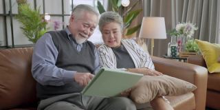 老年亚洲夫妇退休后坐在沙发沙发上视频给家人打电话，用平板电脑设备社交连接家庭隔离呆在家状态秩序概念，幸福老人笑笑快乐
