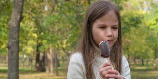 可爱的小女孩在户外吃冰淇淋。可爱的孩子在城市公园散步时享受着美味的冰淇淋