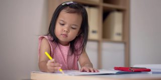 亚洲小女孩在家里用彩色铅笔涂色练习本学习