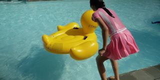 快乐的亚洲女孩跳黄鸭橡皮筏在游泳池期间与家人度假，生活理念。