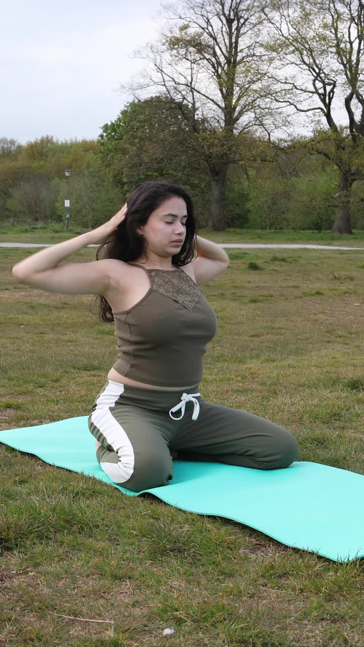 一名年轻女子在公园的绿松石色垫子上练习瑜伽